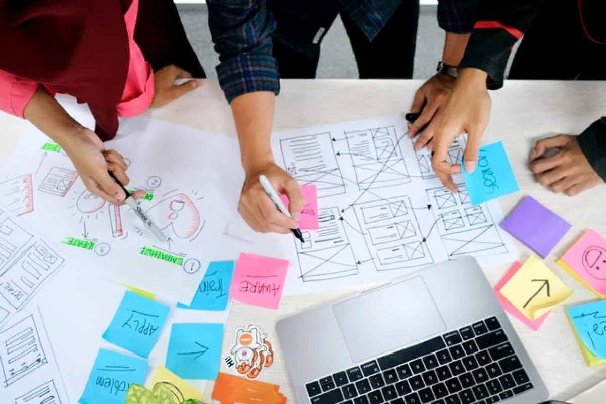 A group of people working over a table that has papers, sticky notes, and a laptop on it.