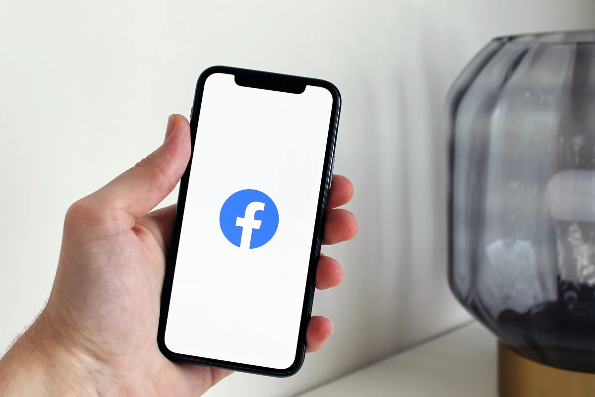 A hand holding a smart phone with a Facebook logo on the screen.