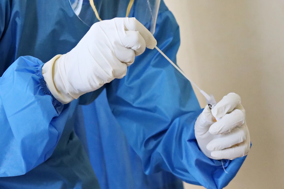 A person wearing a blue medical outfit, with gloved hands putting a covid test into a tube.