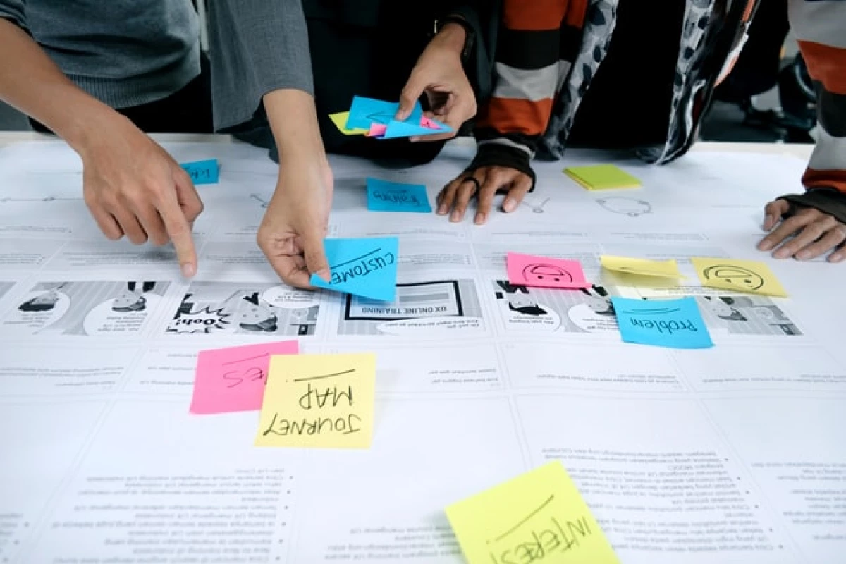 A group of people working over a table with sticky notes, papers, and a laptop.