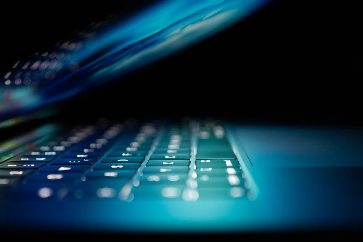 A laptop half closed illuminating the keyboard in a dark room.