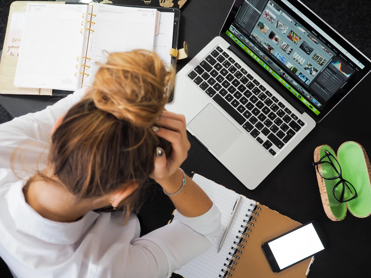 A woman with her hands her head with a laptop and papers on the table around her.