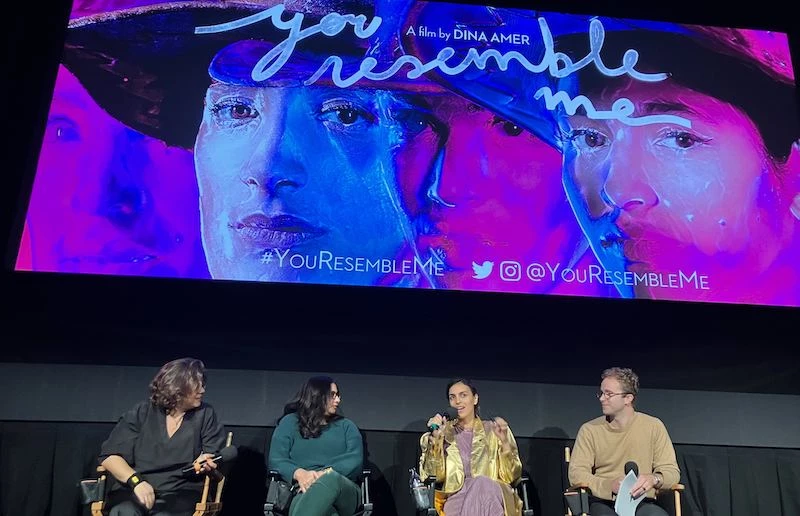 A group of four people speaking on a panel discussion in front of a movie screen.